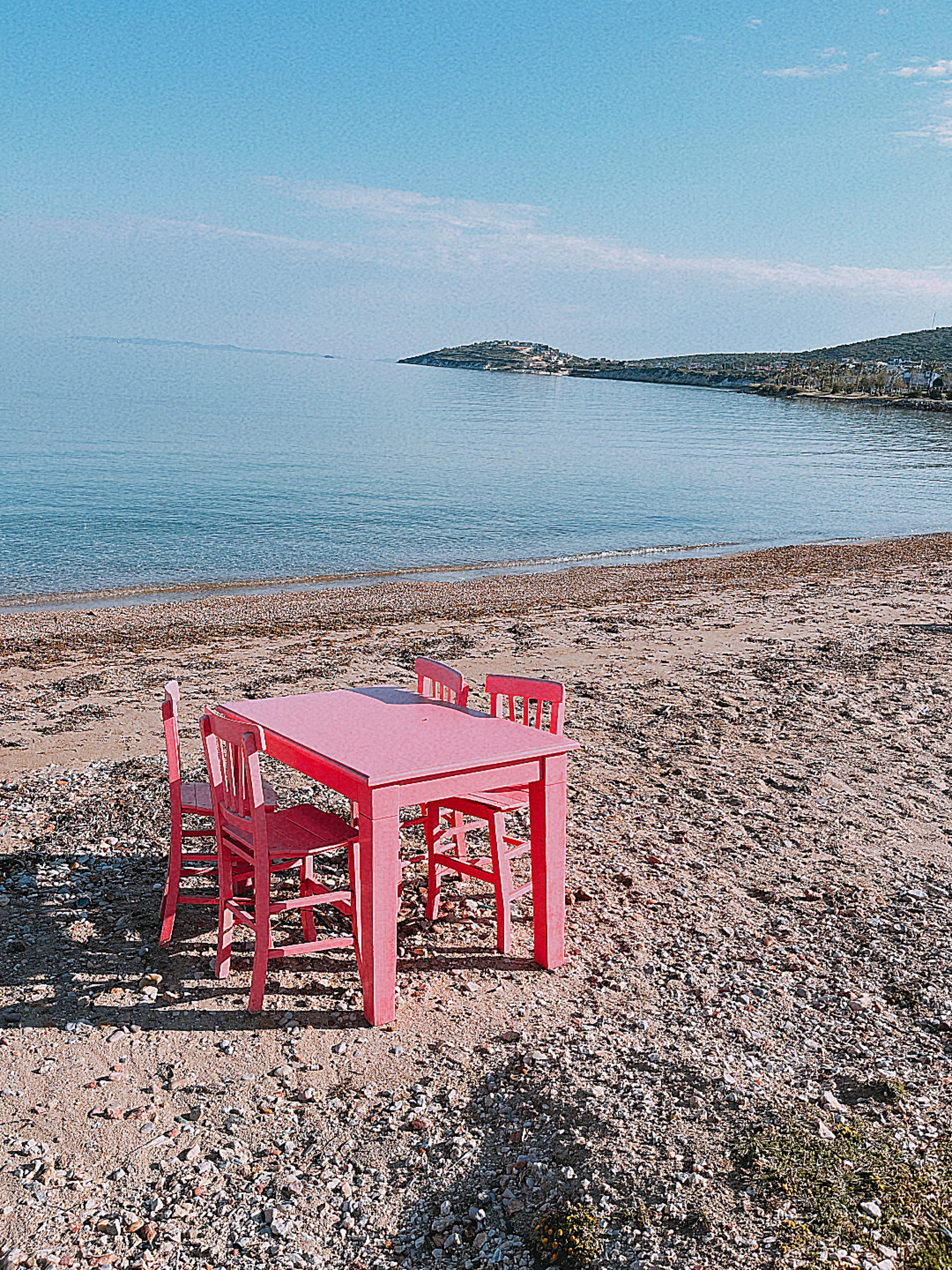 Pink bord og stole på stenstrand med udsigt over havet