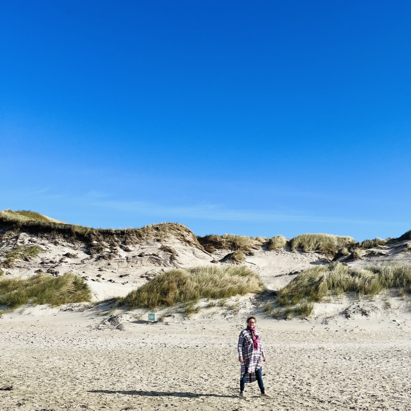 Person på sandstrand med klitter i baggrunden.